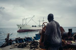<p>一艘中国福建远洋渔船上的非洲本地员工望着不远处的中国转运船驶向达喀尔港口。图片来源：Liu Yuyang / Greenpeace</p>