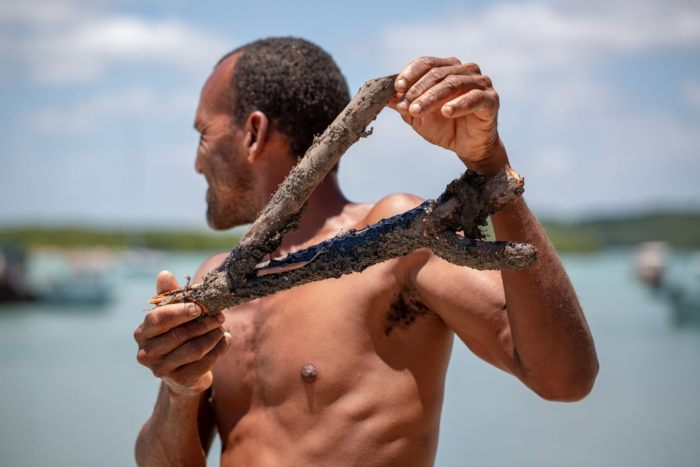 man holds mangrove root covered in oil slick