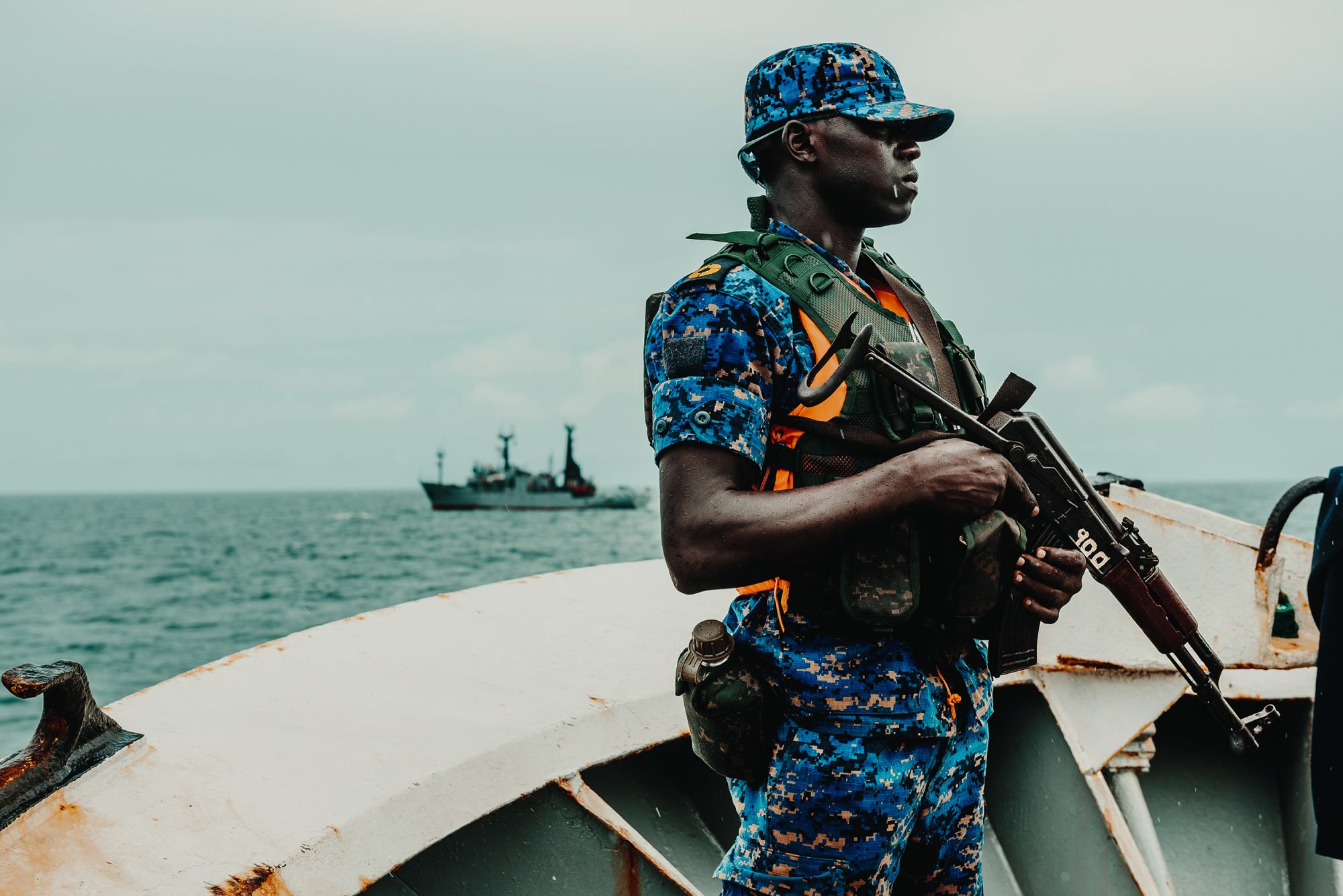 A Gambian Navy sailor stands guard aboard an arrested trawler, with Sea Shepherd’s Sam Simon in the background (Image © Sea Shepherd Global)