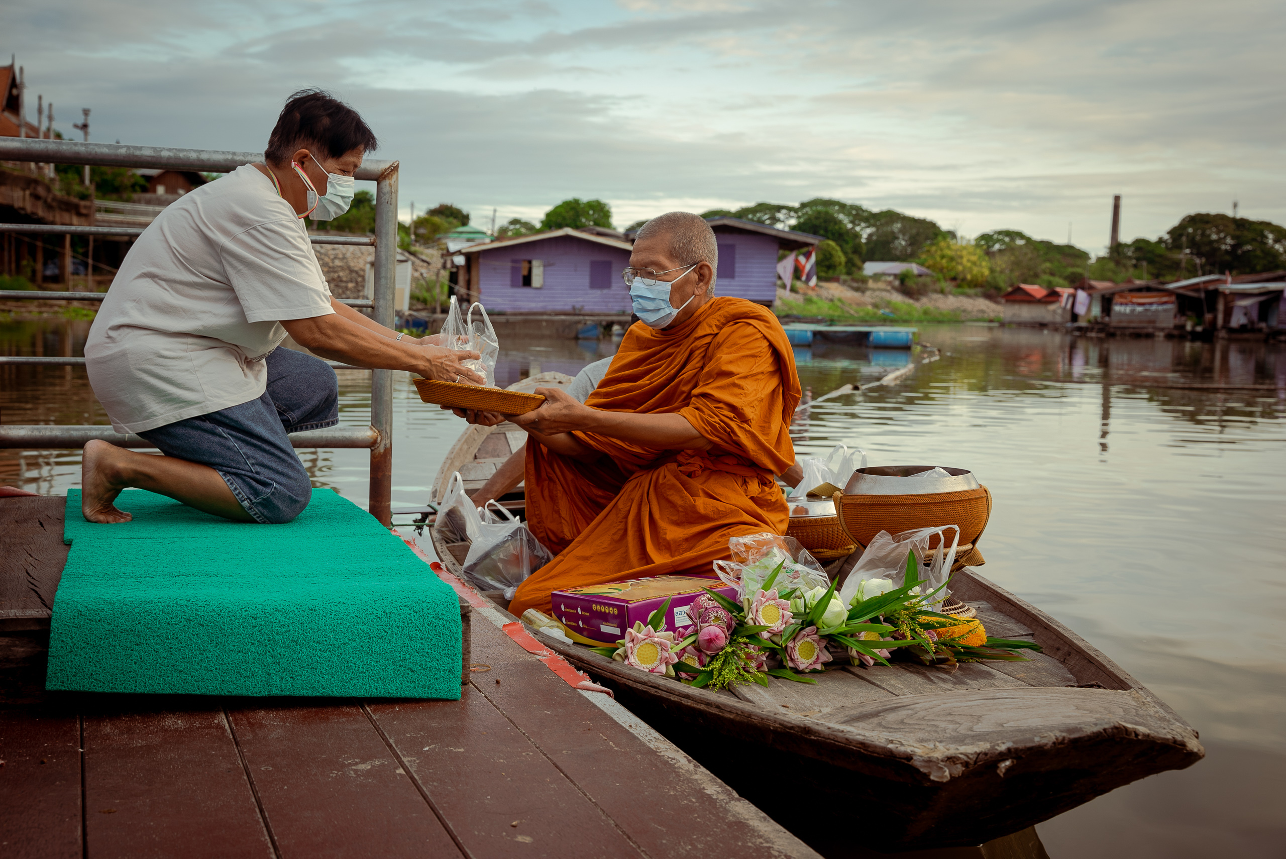 monk on river boat accepting parcel from man on dock