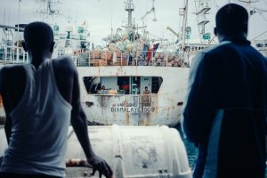 two men seen from behind facing large fishing vessel