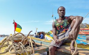 man sitting on small fishing boat with Guinea-Bissau flag