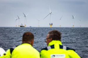Two people in high-vis jackets looking at wind turbines at sea